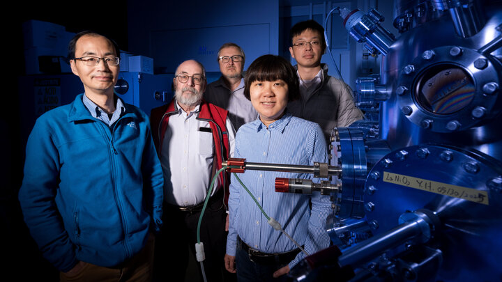 Husker physicists (from left) Xiaoshan Xu, Peter Dowben, Evgeny Tsymbal, Xia Hong and Zuocheng Zhang stand next to an oxide thin film deposition system inside Hong’s lab in Jorgensen Hall. The lighting is blue.