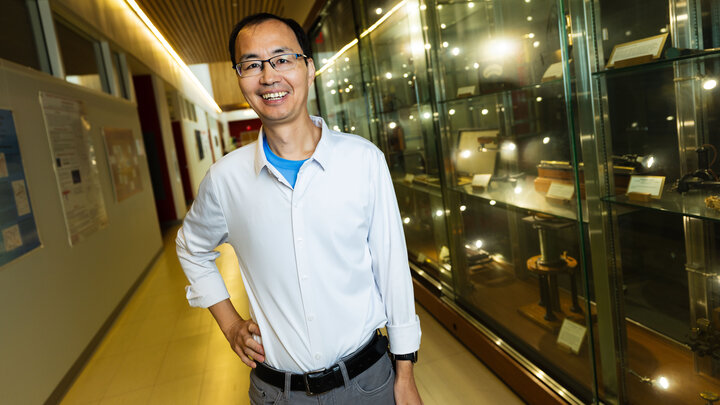 Xiaoshan Xu, Susan J. Rosowski Professor of physics and astronomy, stands in a hallway next to a display case full of antique lab equipment.