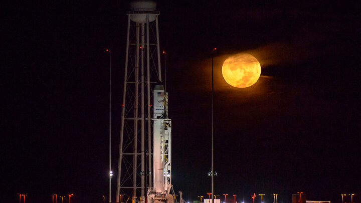 Antares rocket upright in front of the full moon.