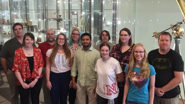 Fellowship recipients and mentors pose in front of scientific instruments display case.